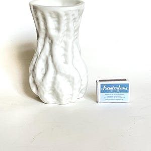 Könnte beinhalten: Weiße Keramikvase mit einer strukturierten, organischen und leicht unebenen Oberfläche. Die Vase ist in Form einer Kalebasse oder einer Erdnuss geformt. Sie ist etwa 25 cm hoch und 10 cm breit. Die Vase steht auf einer weißen Oberfläche. Eine Streichholzschachtel mit dem Text "Freudenhaus Interiors" befindet sich im Hintergrund.