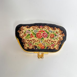 Könnte beinhalten: Eine schwarze Vintage-Geldbörse mit floralem Gobelindesign. Die Geldbörse hat einen goldfarbenen Rahmen und Verschluss mit perlenartigen Akzenten. Der Gobelin zeigt eine farbenfrohe Anordnung von Blumen.