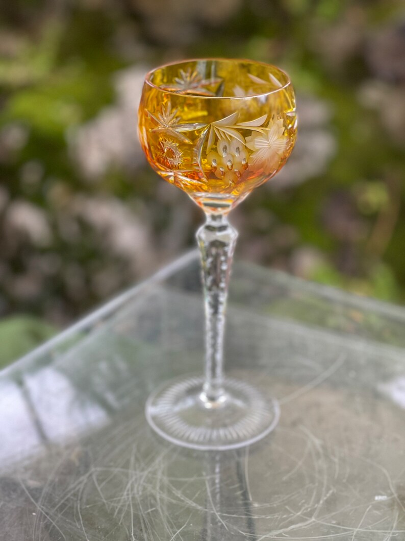 Puede incluir: Un vaso alto y transparente con un dise&ntilde;o de cristal tallado. El vaso tiene una copa redonda y un tallo largo y delgado. La copa es de color &aacute;mbar.