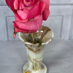 May include: A single pink rose with a green stem in a swirl patterned glass vase with brown, green, and white colors.
