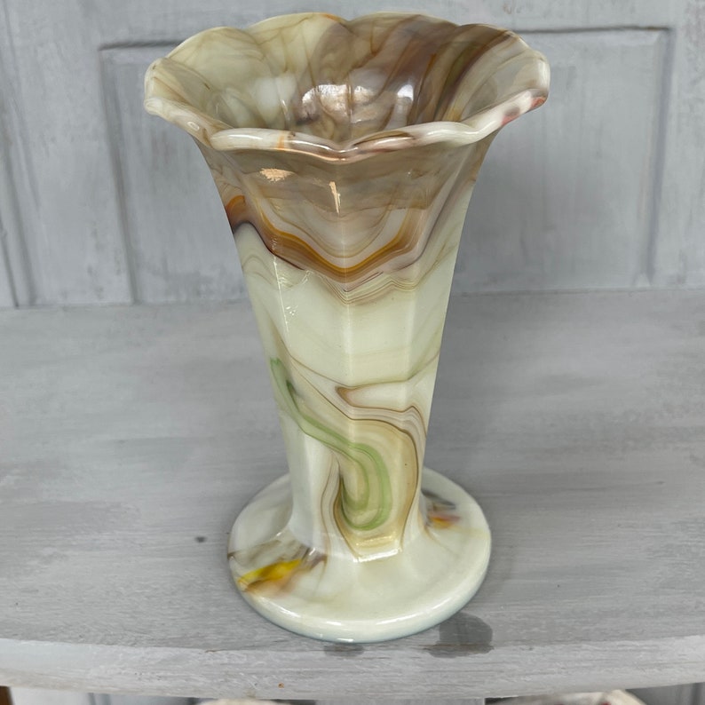 May include: A white, brown, and green swirled glass vase with a scalloped top and a flared base.