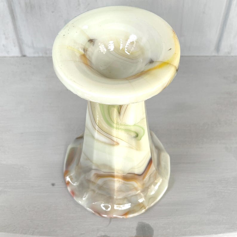 May include: A white, green, and brown swirl glass vase with a wide, flared opening. The vase has a scalloped base.