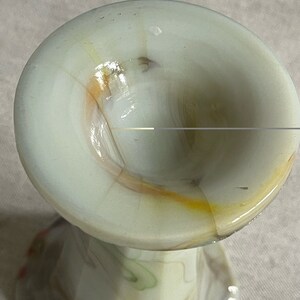 May include: A white glass vase with a swirl pattern in shades of brown, orange, and green. The vase has a wide, round opening and a narrow base.