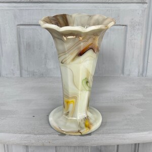 May include: A small, white, brown, and yellow marbled glass vase with a scalloped rim and a flared base.