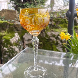 Puede incluir: Un vaso alto de color &aacute;mbar con intrincados dise&ntilde;os de vidrio cortado. El vaso tiene un tallo largo y delgado y un cuenco ancho y redondo. El vaso est&aacute; sobre una superficie de vidrio transparente.