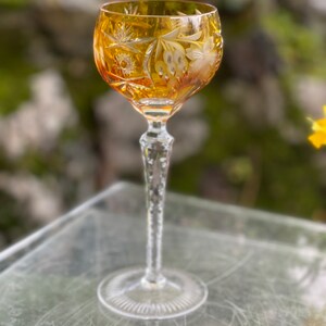 Puede incluir: Un vaso alto de color &aacute;mbar con un dise&ntilde;o de cristal tallado. El vaso tiene un tallo largo y delgado y una copa redonda. La copa est&aacute; decorada con un patr&oacute;n floral.