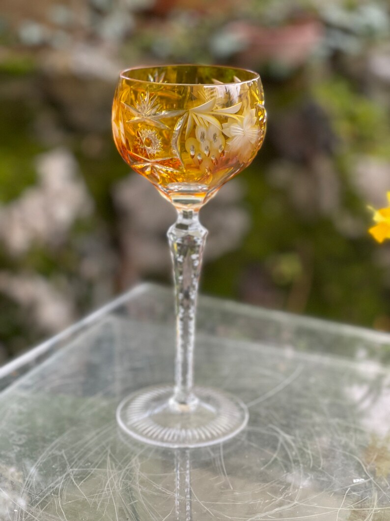 Puede incluir: Un vaso alto de color &aacute;mbar con un dise&ntilde;o de cristal tallado. El vaso tiene un tallo largo y delgado y una copa redonda. La copa est&aacute; decorada con un patr&oacute;n floral.