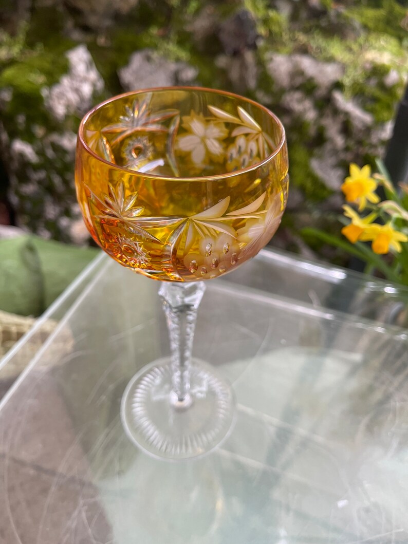 Puede incluir: Una copa de vino de vidrio transparente con un dise&ntilde;o de cristal tallado. La copa tiene un tono &aacute;mbar y un tallo largo.