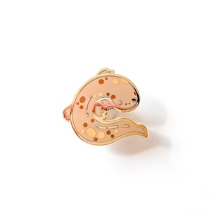 May include: Gold-coloured enamel pin featuring a cartoon illustration of a brown and white spotted salamander with a curled tail.