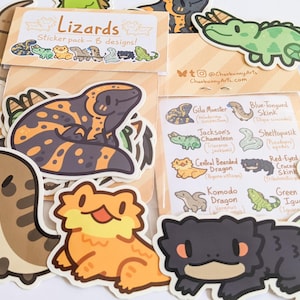 May include: A sticker pack featuring eight cartoon lizard designs. The packaging displays the text "Lizards sticker pack - 8 designs!" and includes illustrations of a Gila Monster, Blue-Tongued Skink, Jackson's Chameleon, Sheltopusik, Central Bearded Dragon, Red-Eyed Crocodile Skink, Komodo Dragon, and Green Iguana.