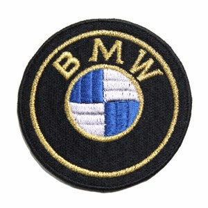 May include: A black and gold embroidered patch with the BMW logo. The logo is a white and blue propeller design with the letters BMW in gold around the outside.