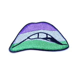 May include: An embroidered patch in the shape of a pair of lips with a green, white, and purple color scheme. The lips are slightly parted, revealing a black outline of teeth.