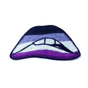 May include: An embroidered patch in the shape of a pair of lips, featuring black, grey and purple stripes. The lips are open and the colours are arranged in a horizontal stripe pattern.