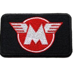 Peut inclure: Un écusson brodé noir avec un cercle rouge et une lettre blanche "M" avec des ailes. Le cercle a un contour blanc.