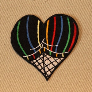 May include: A black heart-shaped embroidered patch featuring two hot air balloons in a basket. The balloons are striped with red, yellow, green, blue, and white.