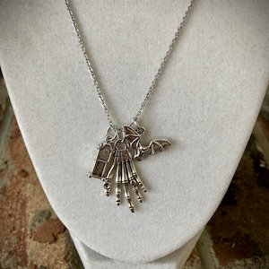 May include: A silver necklace with a skeleton hand charm, a bat charm, and a small coffin charm.
