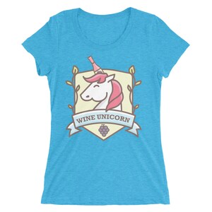 Puede incluir: Una camiseta de mujer azul turquesa con una ilustraci&oacute;n de dibujos animados de un unicornio con una botella de vino en la cabeza. La ilustraci&oacute;n est&aacute; rodeada de un escudo con el texto "Wine Unicorn".
