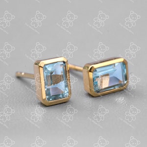 Puede incluir: Un par de pendientes de oro con piedras rectangulares de color azul claro. Los pendientes tienen un diseño simple y elegante.