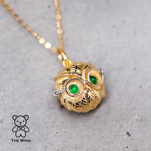 Könnte beinhalten: Eine goldene Eulen-Anhängerkette mit grünen Augen und einer Brille. Die Eule ist mit einer strukturierten Oberfläche verziert und hängt an einer zarten goldenen Kette.