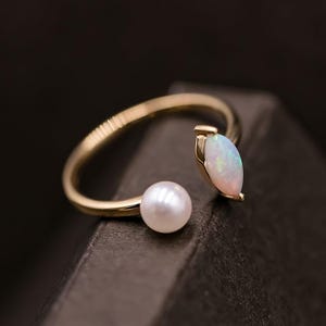 May include: A gold ring with a white opal and a pearl. The ring is open on one side and has a delicate design.