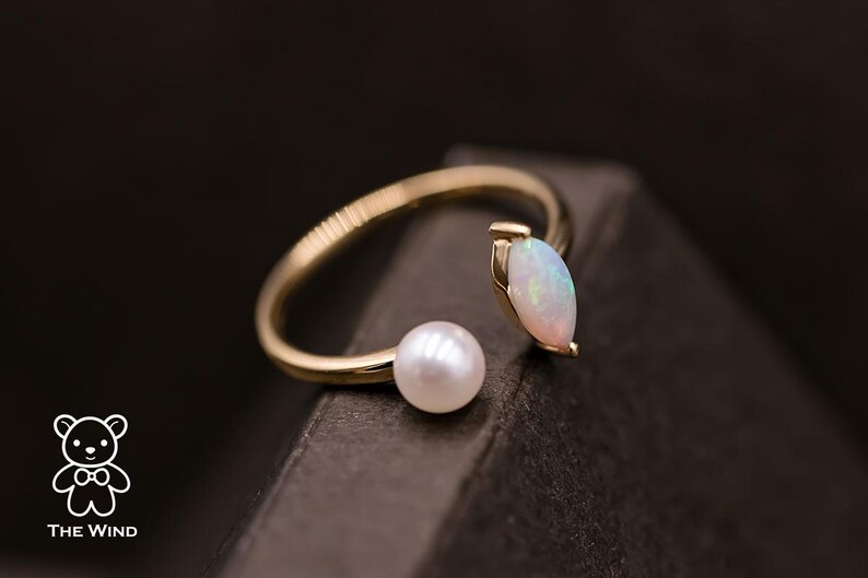 May include: A gold ring with a white opal and a pearl. The ring is open on one side and has a delicate design.
