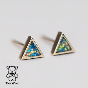 Puede incluir: Un par de pendientes de oro en forma de triángulo con piedras de ópalo iridiscente. Los pendientes son pequeños y delicados.