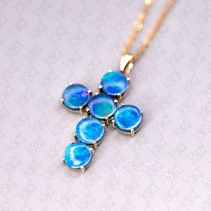 Może przedstawiać: Złoty łańcuszek z zawieszką w kształcie krzyża. Krzyż wykonany jest z siedmiu okrągłych niebieskich opali.