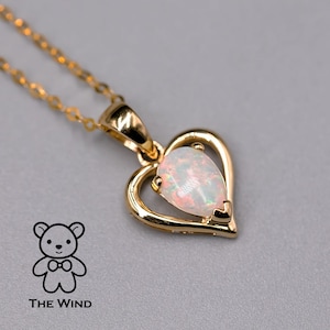 Puede incluir: Un collar de oro con un colgante en forma de corazón adornado con una piedra de ópalo blanco. El colgante está en una cadena de oro delicada.