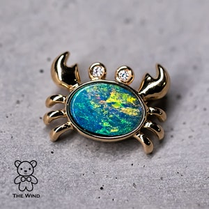 Pode incluir: Um amuleto de caranguejo de ouro com uma pedra de opala verde e azul e dois pequenos diamantes.