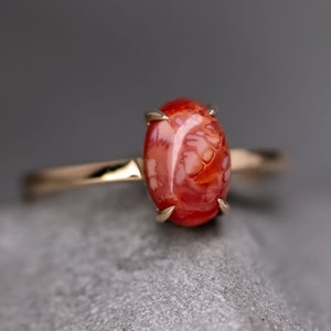 Könnte beinhalten: Ein goldener Ring mit einem ovalen roten und weißen Edelstein. Der Edelstein hat ein einzigartiges, wirbelndes Muster.