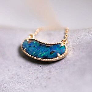 Puede incluir: Un collar de cadena de oro con un gran colgante de ópalo azul. El ópalo está engastado en un bisel de oro y tiene un borde festoneado.