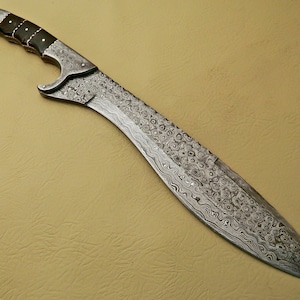 May include: A silver sword with a patterned blade and a black handle. The sword has a curved blade and a pointed tip.