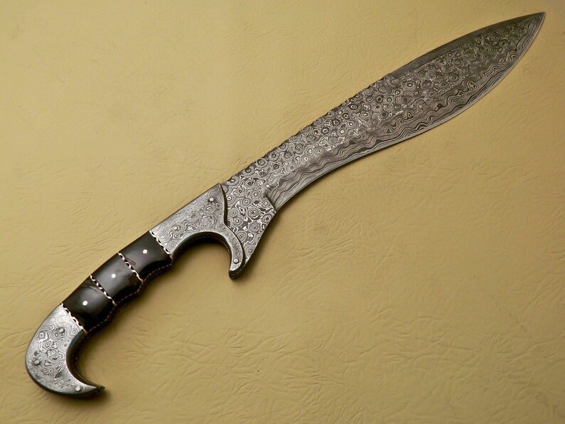May include: A silver-colored, Damascus steel sword with a black handle. The blade is curved and has a decorative pattern. The handle is made of wood and has a black finish.