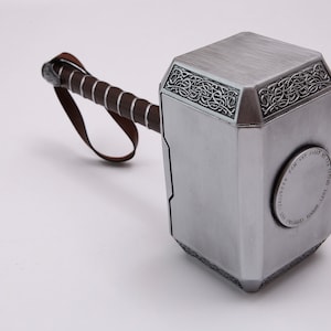 Pu&ograve; includere: Un martello color argento con un manico in pelle marrone. Il martello presenta disegni intricati sulla testa e il testo "Whosoever holds this hammer, if he be worthy, shall possess the power of Thor." &egrave; inciso sul lato.