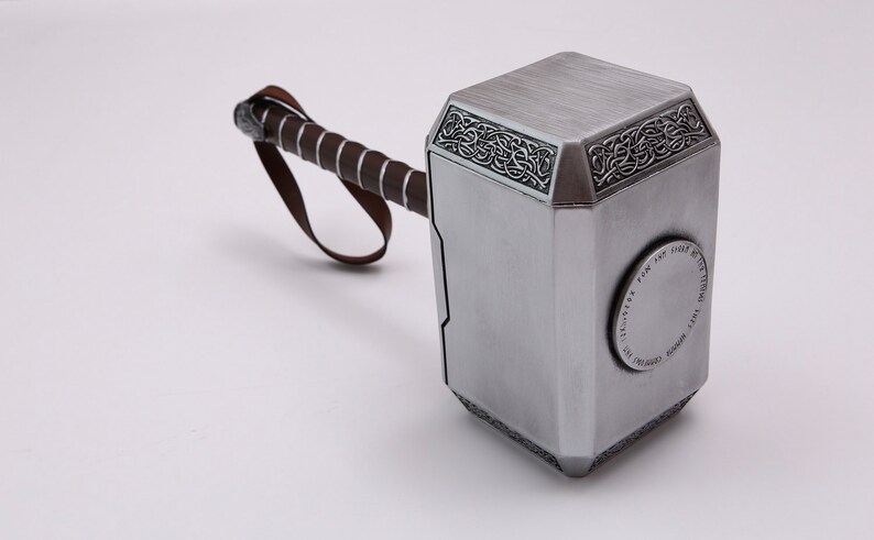 Pu&ograve; includere: Un martello color argento con un manico in pelle marrone. Il martello presenta disegni intricati sulla testa e il testo "Whosoever holds this hammer, if he be worthy, shall possess the power of Thor." &egrave; inciso sul lato.