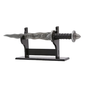 May include: A silver dagger with a black handle and a skull design on the pommel. The dagger is displayed on a black wooden stand. The blade is engraved with the words "Vampire Slayer".