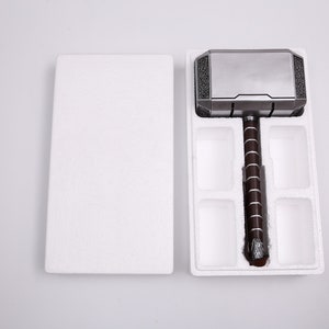 Pu&ograve; includere: Una replica in argento e nero del martello di Thor, Mjolnir, &egrave; esposta in un imballaggio di schiuma bianca. Il martello ha un manico rivestito in pelle marrone.