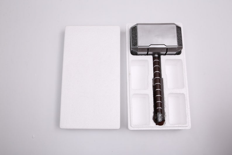 Pu&ograve; includere: Una replica in argento e nero del martello di Thor, Mjolnir, &egrave; esposta in un imballaggio di schiuma bianca. Il martello ha un manico rivestito in pelle marrone.