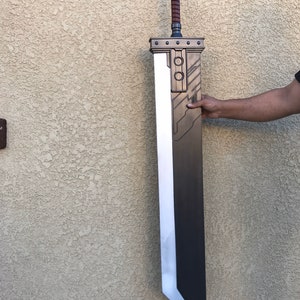 May include: A large, black and silver sword with a brown handle. The sword has a detailed design on the blade and a silver blade.