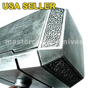 Pu&ograve; includere: Una replica argentata del martello di Thor, Mjolnir, con dettagli intricati e una superficie testurizzata. Il martello ha un manico nero e una testa argentata con un disegno di linee intrecciate.