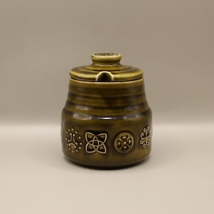 May include: A green ceramic sugar bowl with a lid and a spout. The bowl features a Celtic knot design and other geometric patterns.