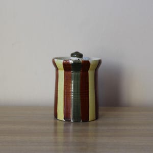May include: A striped ceramic jar with a lid. The jar is decorated with yellow, brown, and green stripes.