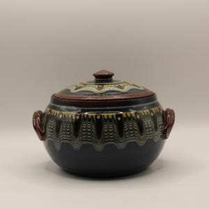 May include: A dark blue ceramic casserole dish with a lid. The dish has a brown rim and a white and brown geometric pattern around the top.
