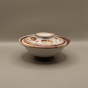 May include: A white ceramic bowl with a brown rim and a brown floral design. The bowl has a lid with a matching design.