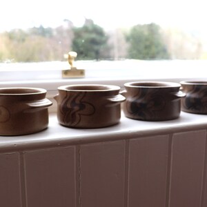 May include: Set of four brown ceramic bowls with a swirl pattern. The bowls have two handles on each side.