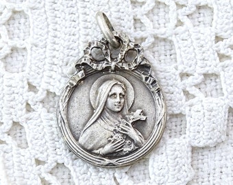 May include: Silver pendant featuring a religious image of the Virgin Mary holding a rosary. The pendant is ornate with a detailed design and a delicate bow at the top.