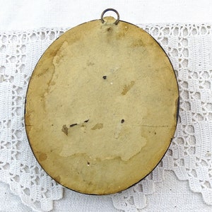 May include: The back of a round, wooden picture frame with a metal hanging hook. The frame is painted a light brown colour and has a worn, aged appearance.