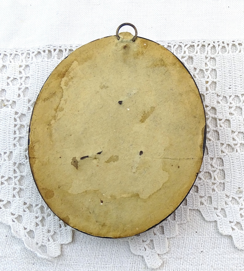 May include: The back of a round, wooden picture frame with a metal hanging hook. The frame is painted a light brown colour and has a worn, aged appearance.
