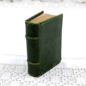 May include: A small, antique book bound in a dark green leather cover. The spine features three raised horizontal bands, and the top edges of the pages are gilded, showing a metallic gold finish when viewed from the top of the upright volume.