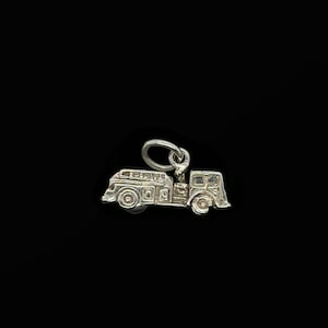 Può includere: Un piccolo ciondolo color argento a forma di camion dei pompieri vintage. Il ciondolo presenta dettagli come ruote, finestre e una scala. È sospeso da un piccolo anello, pronto per essere aggiunto a una collana o un braccialetto.
